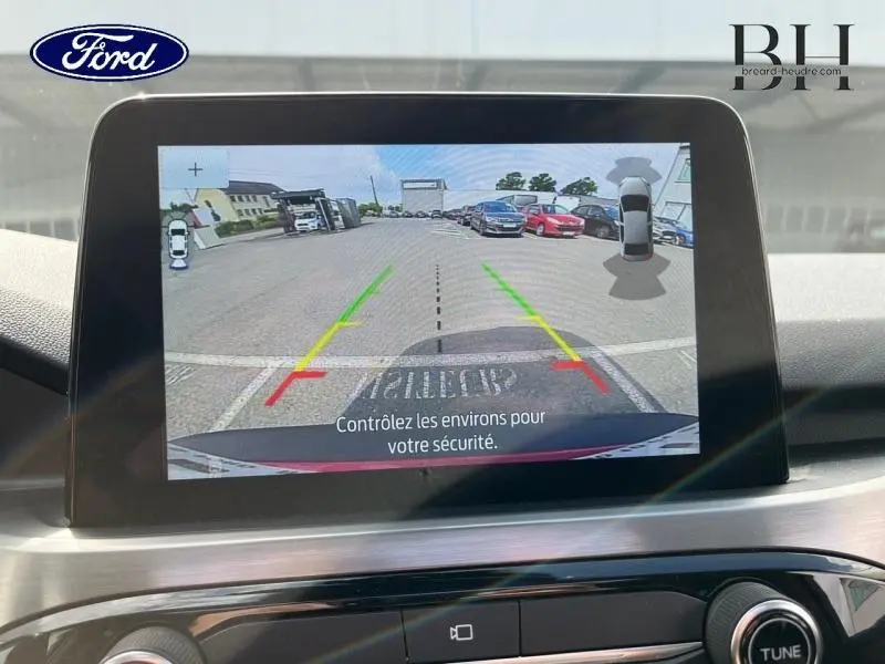 Écran tactile intérieur du Ford Kuga montrant la caméra de recul avec lignes de guidage colorées et vue arrière du parking.