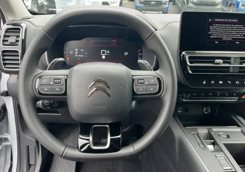 Vue intérieure centrée sur le volant cuir multifonctions et le tableau de bord numérique du Citroën C5 Aircross blanc okénite.