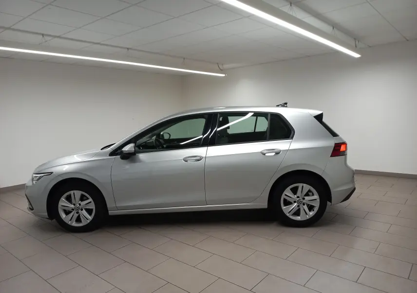 Vue de profil côté gauche d'une Volkswagen Golf 2.0 TDI 116 DSG7 Life Plus 2023 en reflet d'argent dans un intérieur neutre.