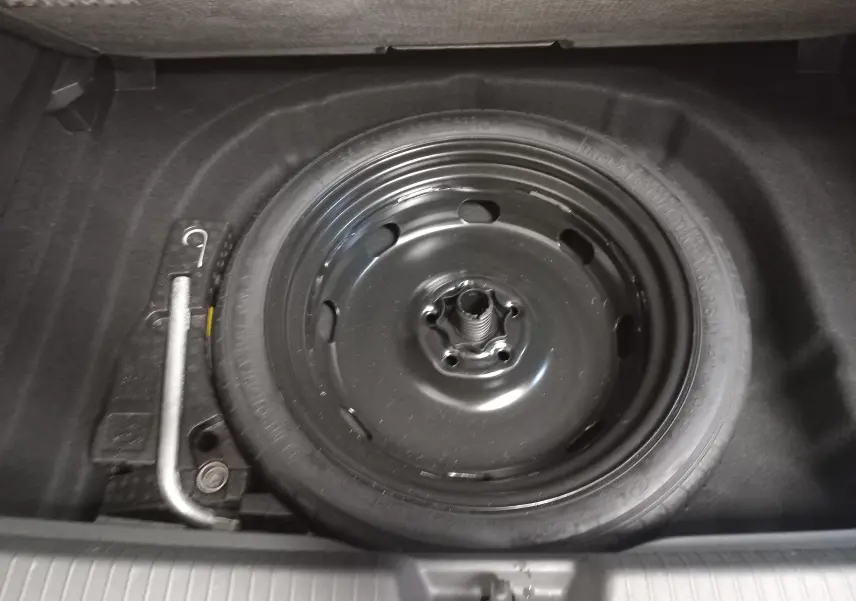 Roue de secours noire dans le coffre d'une Volkswagen Golf 2023, vue plongeante sur le pneu et outil de levage.