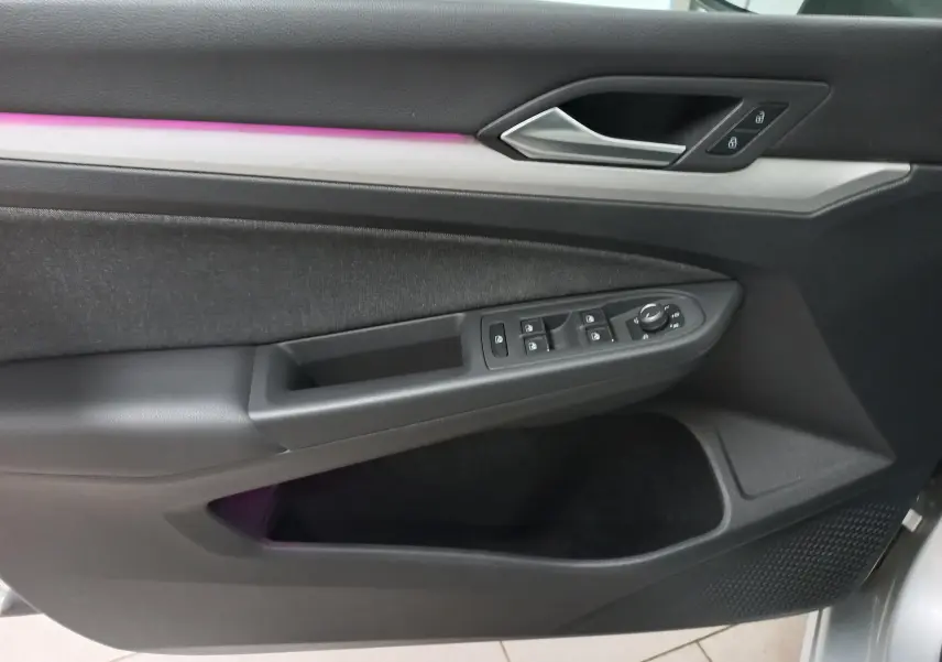 Intérieur côté gauche de la porte d'une Volkswagen Golf 2023 argent, avec commandes de vitres et éclairage d'ambiance violet.