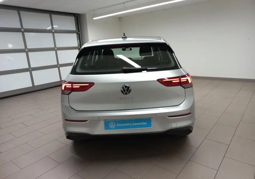 Vue arrière d'une Volkswagen Golf 2.0 TDI 116 DSG7 Life Plus 2023 en reflet d'argent avec feux arrière allumés dans un garage.