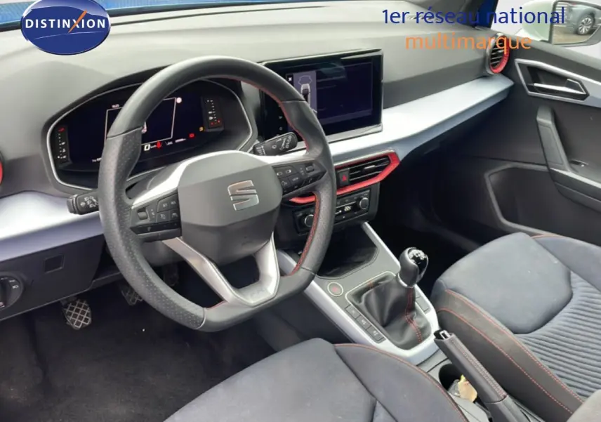 Vue intérieure côté conducteur du tableau de bord et volant de la SEAT Arona 2025 avec finitions rouges et volant cuir.