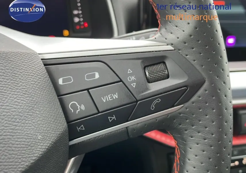 Gros plan sur les commandes à gauche du volant en cuir perforé noir avec surpiqûres rouges du SEAT Arona 2025.