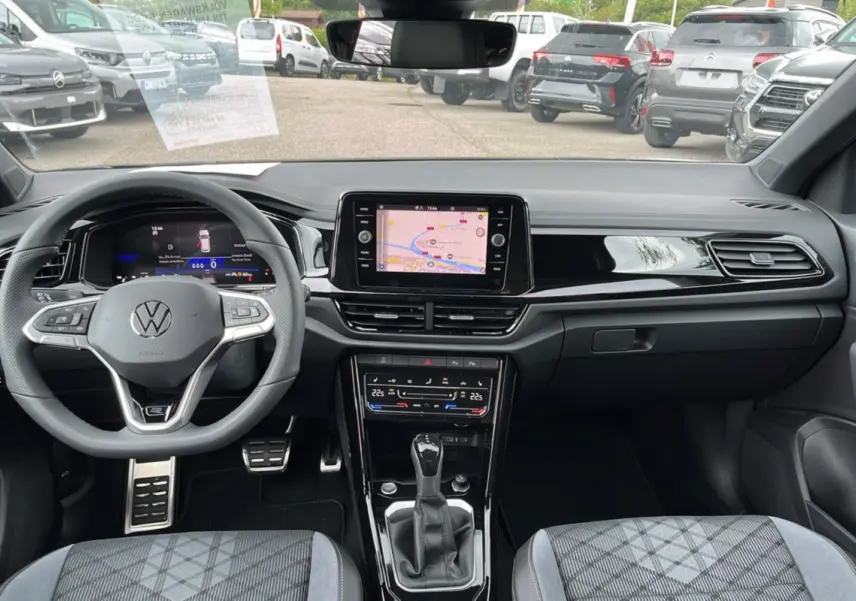Vue intérieure avant du Volkswagen T-Roc gris indium, avec tableau de bord numérique et écran tactile central affichant la navigation GPS.