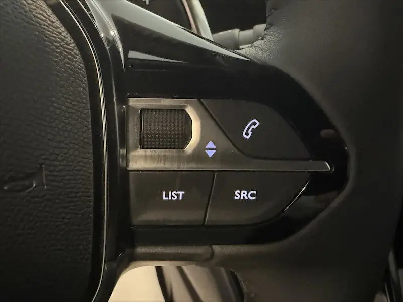 Gros plan sur les commandes gauche du volant noir du Peugeot 2008 Hybrid 145ch, boutons LIST, SRC et téléphone.