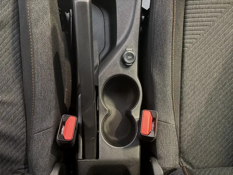 Vue plongeante sur la console centrale noire avec porte-gobelets et ceintures rouges entre les sièges tissu noir du Peugeot 2008 hybride.