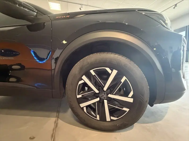 Gros plan sur la roue avant droite et la carrosserie noire métal du Peugeot 2008 Hybrid 145ch Style 2025, avec jante design bicolore.