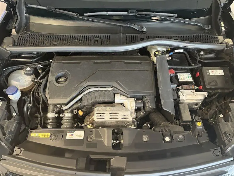 Vue plongeante sur le compartiment moteur noir d'un Peugeot 2008 Hybrid 145ch, montrant les composants hybrides et batterie.