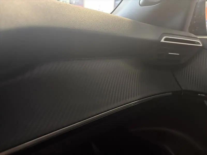 Détail de la planche de bord noire avec texture carbone et sortie d'air côté passager du Peugeot 2008 Hybrid 2025.