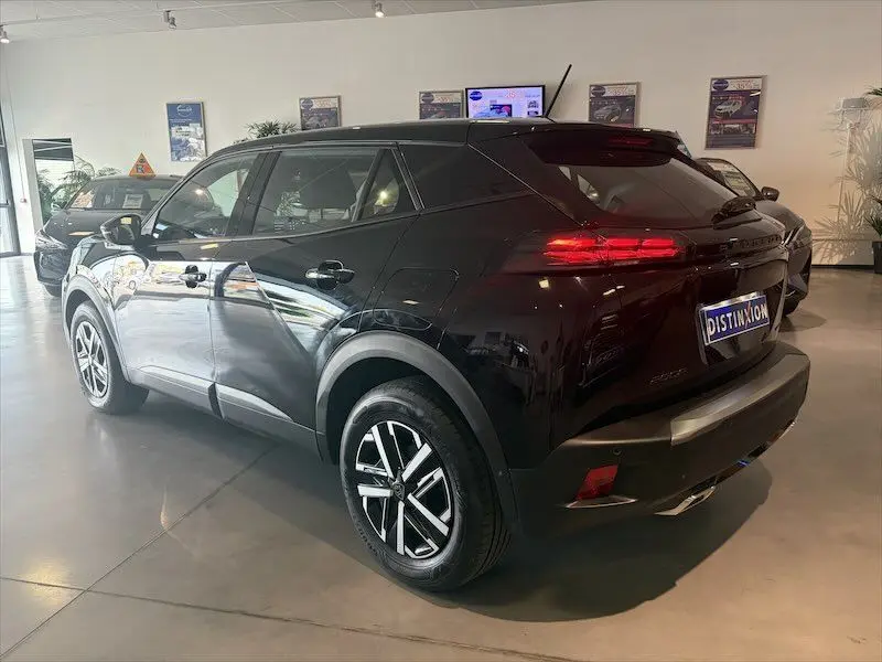Vue 3/4 arrière droite d’un Peugeot 2008 noir métal hybride 2025 en showroom avec feux arrière allumés.