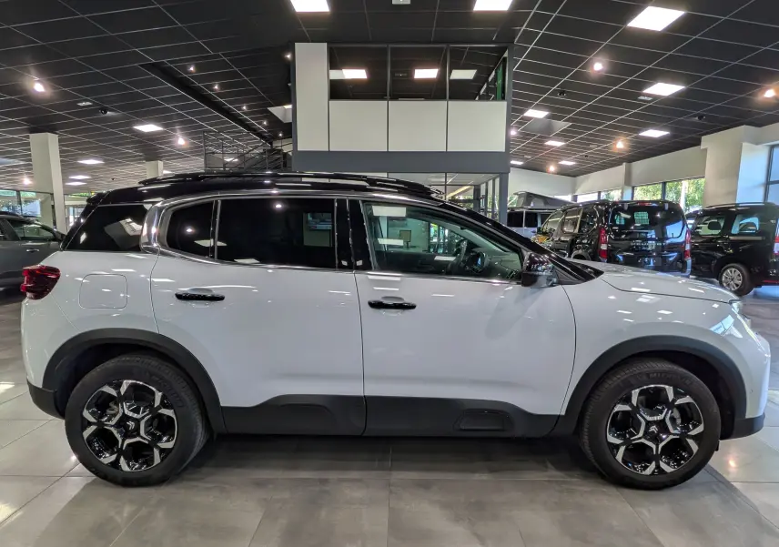 Vue latérale droite d'un Citroën C5 Aircross 2025 blanc Okénite avec toit noir et jantes noires en concession.