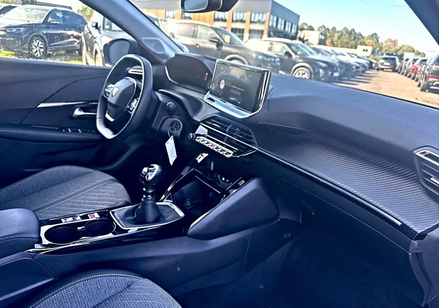 Intérieur de Peugeot 208 1.2 100 allure noir, vue côté conducteur, tableau de bord avec écran tactile et boîte manuelle.