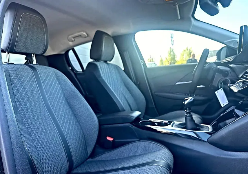 Intérieur de la Peugeot 208 1.2 100 Allure 2025, vue côté droit sur les sièges tissu gris et la boîte manuelle.