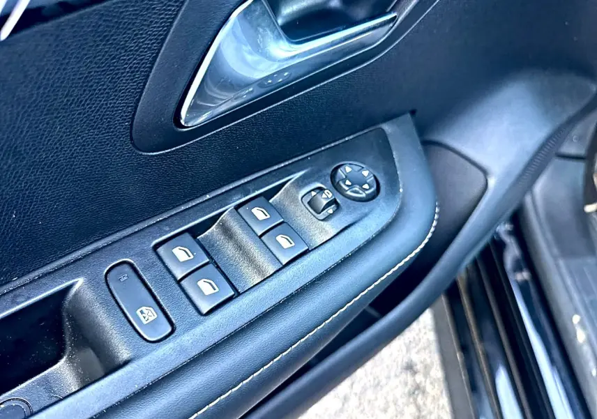 Vue rapprochée du panneau de commandes des vitres et rétroviseurs côté conducteur d’une Peugeot 208 noire.