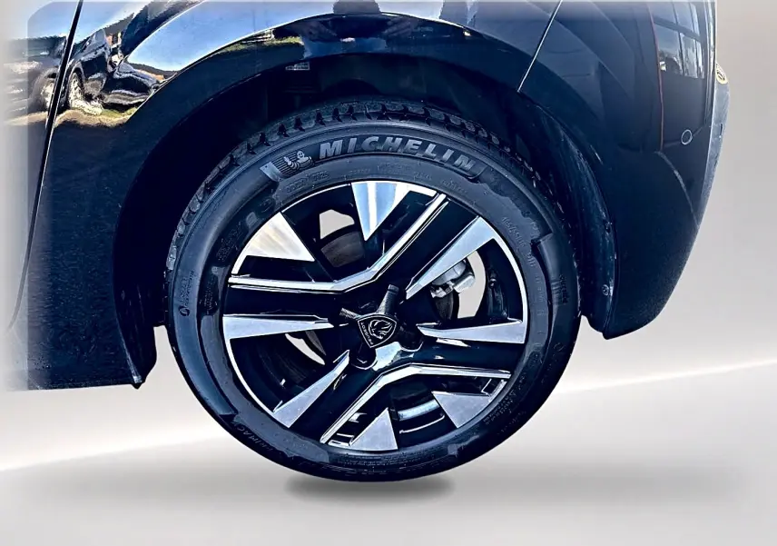 Gros plan sur la roue avant gauche noire d'une Peugeot 208 1.2 100 allure avec jante alu bicolore et pneu Michelin.
