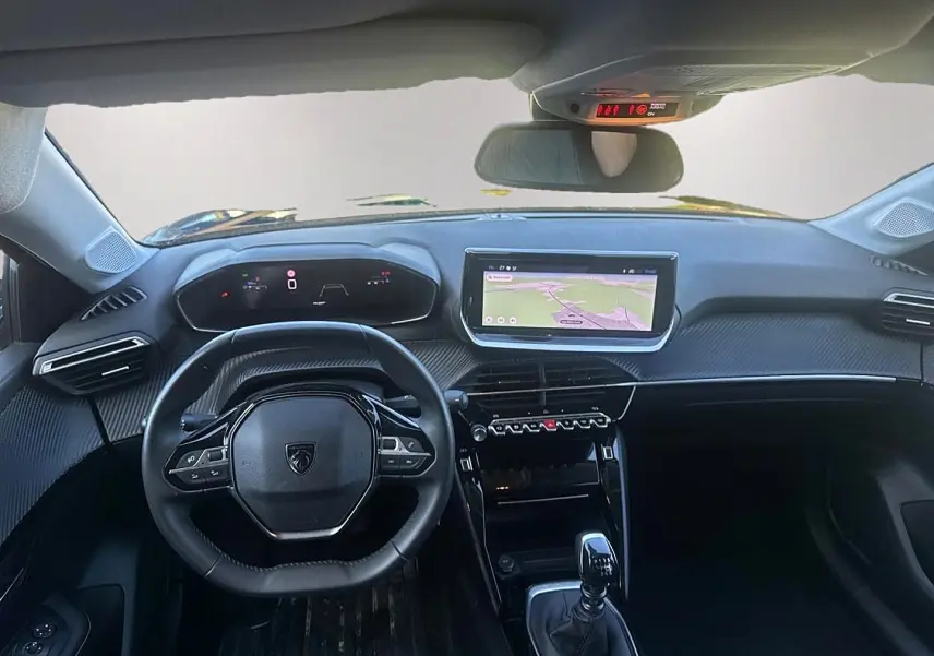 Vue intérieure avant de la Peugeot 208 1.2 100 Allure 2025, tableau de bord noir avec écran tactile et volant compact.