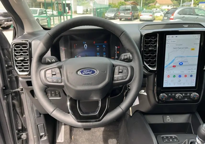 Vue intérieure centrée sur le volant cuir multifonctions et l’écran tactile vertical du Ford Ranger gris carbone 2025.