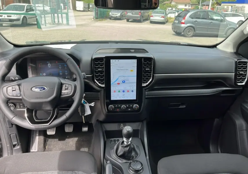 Vue intérieure frontale du Ford Ranger gris carbone 2025, avec volant multifonctions et écran tactile vertical.