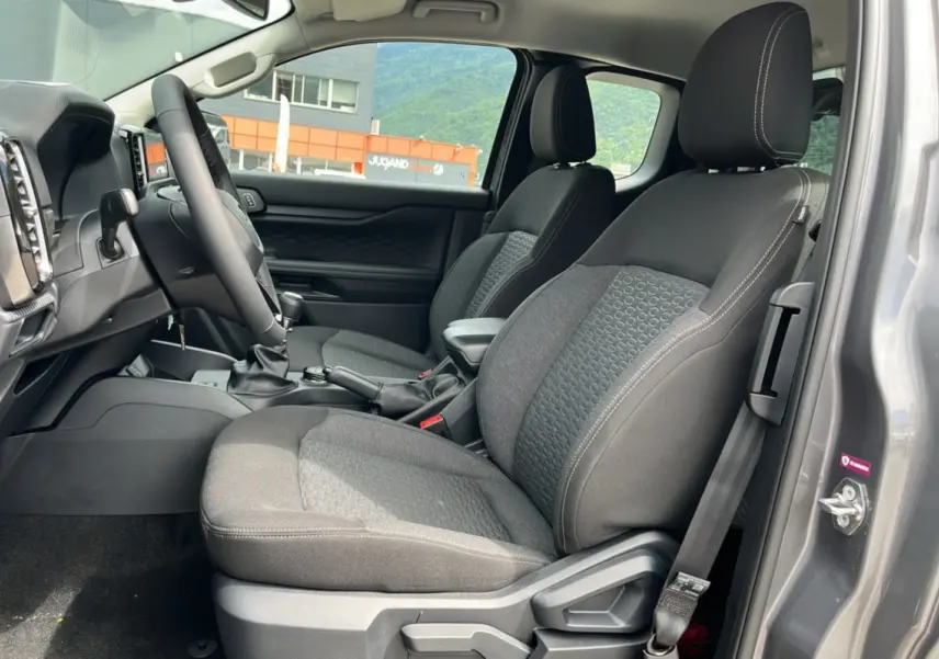 Vue intérieure côté conducteur du Ford Ranger gris carbone 2025, montrant les sièges avant en tissu et le volant multifonctions cuir.