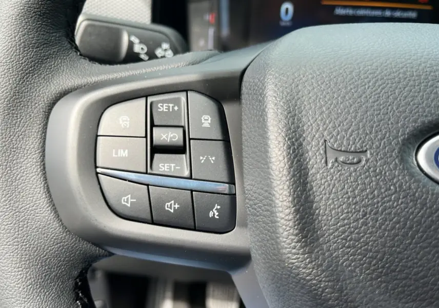Gros plan sur les commandes multifonctions à gauche du volant cuir du Ford Ranger gris carbone 2025.