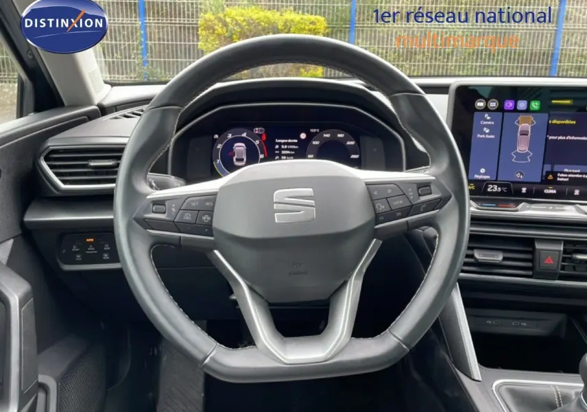 Vue intérieure centrée sur le volant cuir multifonction d'une SEAT LEON ST 2025, avec tableau de bord digital et écran tactile.