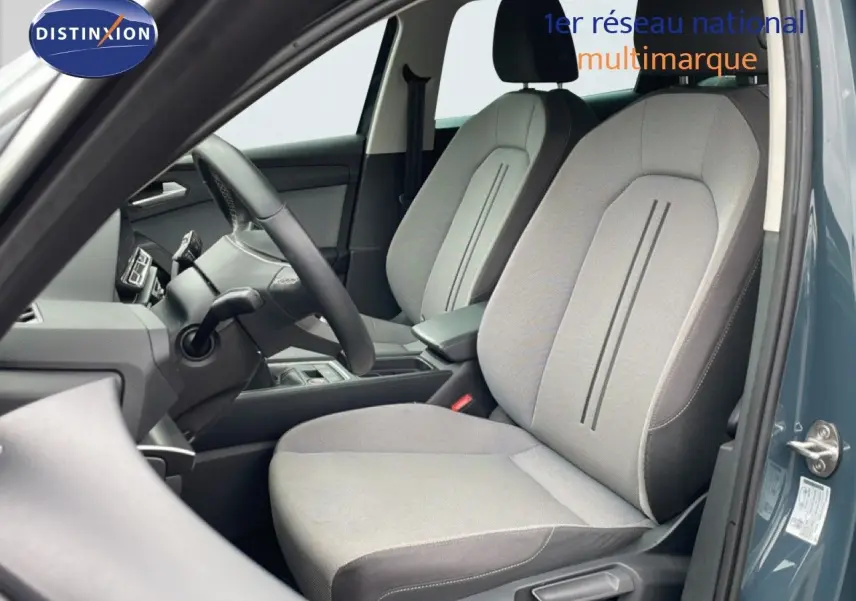 Vue intérieure côté conducteur du SEAT LEON ST gris métallique, montrant les sièges tissu gris clair et le volant multifonction.