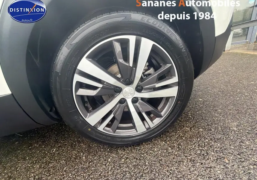 Gros plan sur la jante alliage avant droite du Peugeot 3008 Hybrid blanc, avec logo Peugeot au centre.