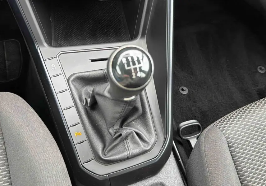 Gros plan sur le levier de vitesses manuel noir de la Volkswagen Polo Business 2021, entouré de sièges gris à motifs.