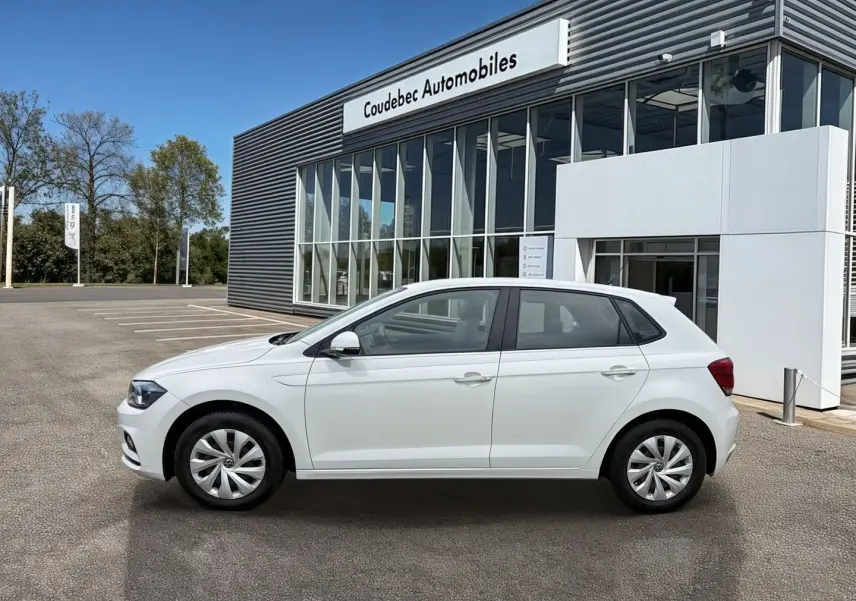 Vue latérale droite d'une Volkswagen Polo Business blanche stationnée devant un bâtiment moderne avec jantes en acier et enjoliveurs intégrals.