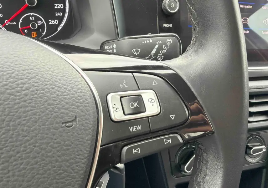 Gros plan sur le volant noir de la Volkswagen Polo Business 2021 avec commandes multifonctions et tableau de bord partiel.
