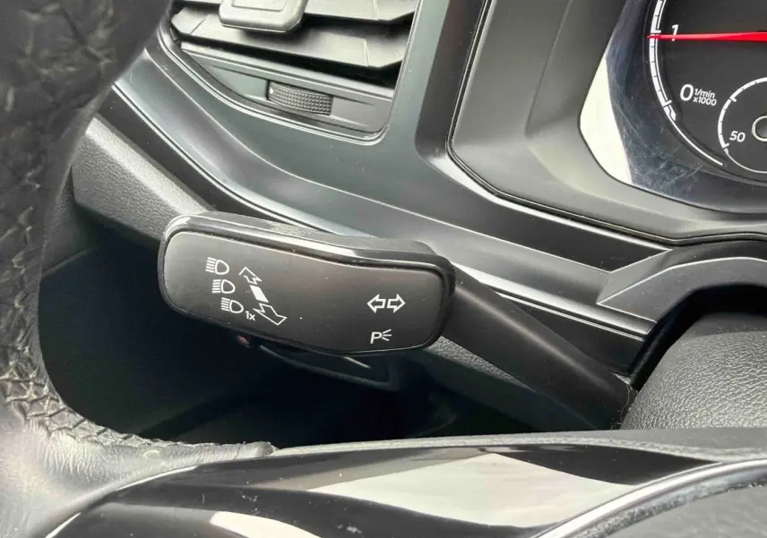 Gros plan sur la manette de clignotants noire à gauche du volant dans l’habitacle d’une Volkswagen Polo Business blanche.
