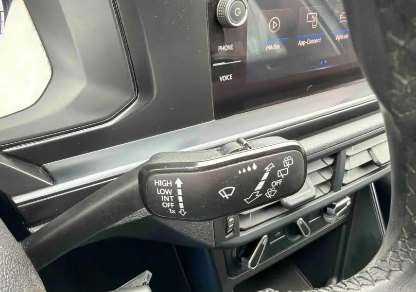 Gros plan sur la commande d’essuie-glace côté gauche du tableau de bord noir d’une Volkswagen Polo blanche.