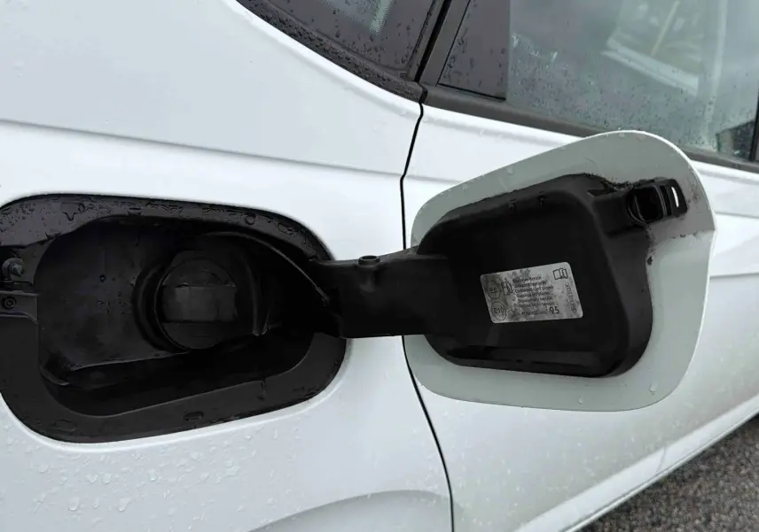 Gros plan sur la trappe à carburant ouverte côté gauche d’une Volkswagen Polo Business blanche sous la pluie.