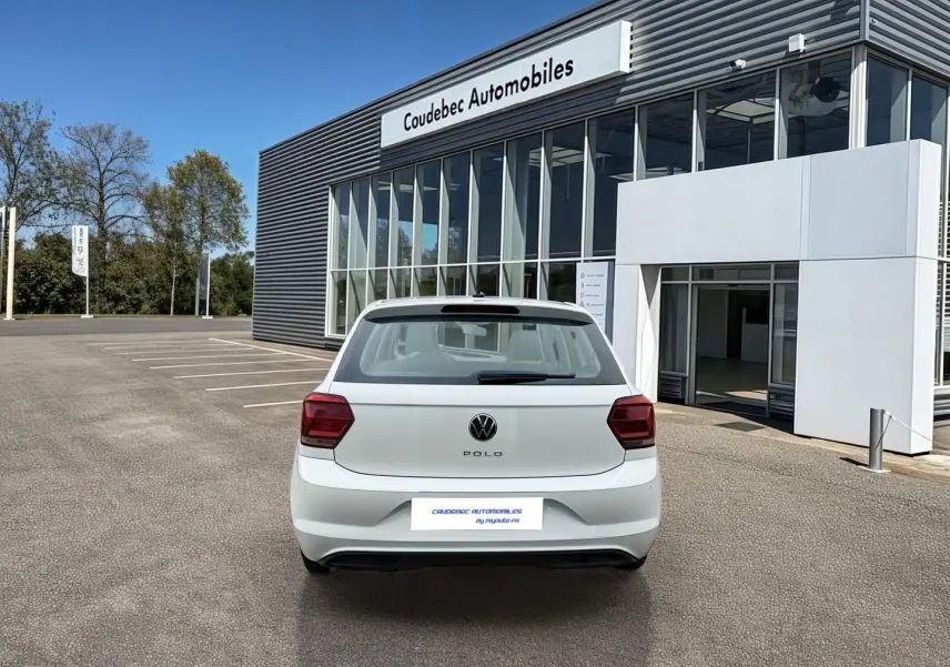 Vue arrière d'une Volkswagen Polo Business blanche stationnée devant un bâtiment commercial moderne.