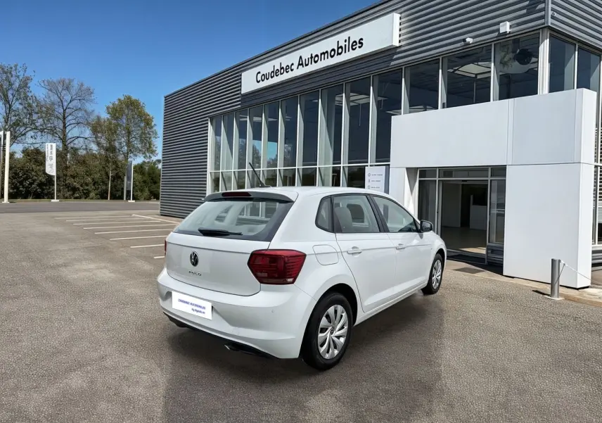 Volkswagen Polo Business blanche vue 3/4 arrière droit devant un bâtiment commercial.