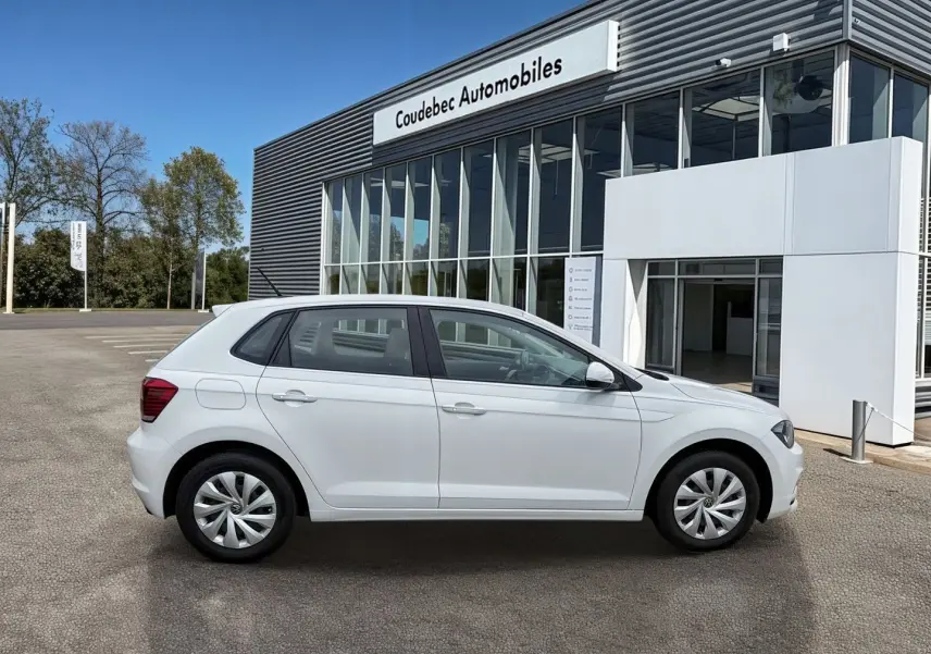 Vue de profil côté gauche d'une Volkswagen Polo Business blanche stationnée devant un bâtiment commercial.