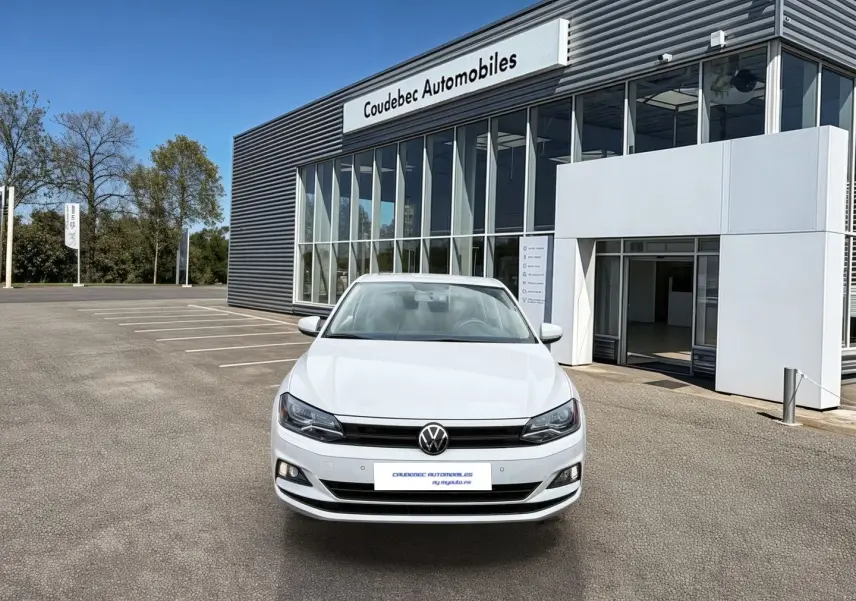 Volkswagen Polo Business blanche vue de face, stationnée devant un bâtiment commercial moderne.