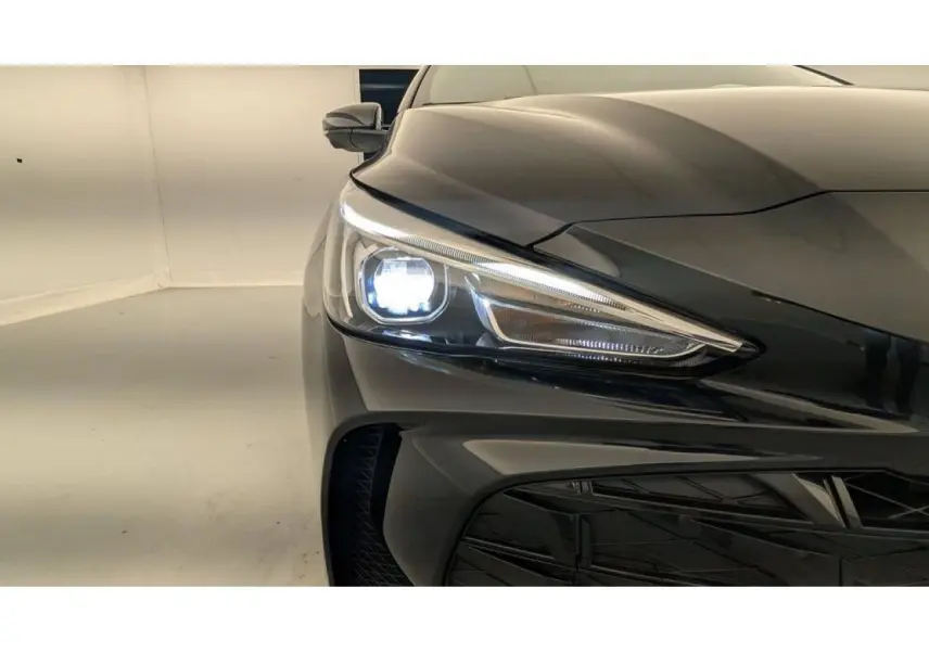 Gros plan sur l'avant droit noir métallisé du MG3 1.5 Hybrid+ 195 Luxury avec phare allumé et calandre visible.