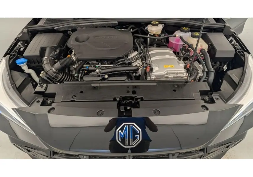 Vue plongeante sur le moteur hybride d'une MG3 1.5 Hybrid+ noire, capot ouvert avec logo MG visible.