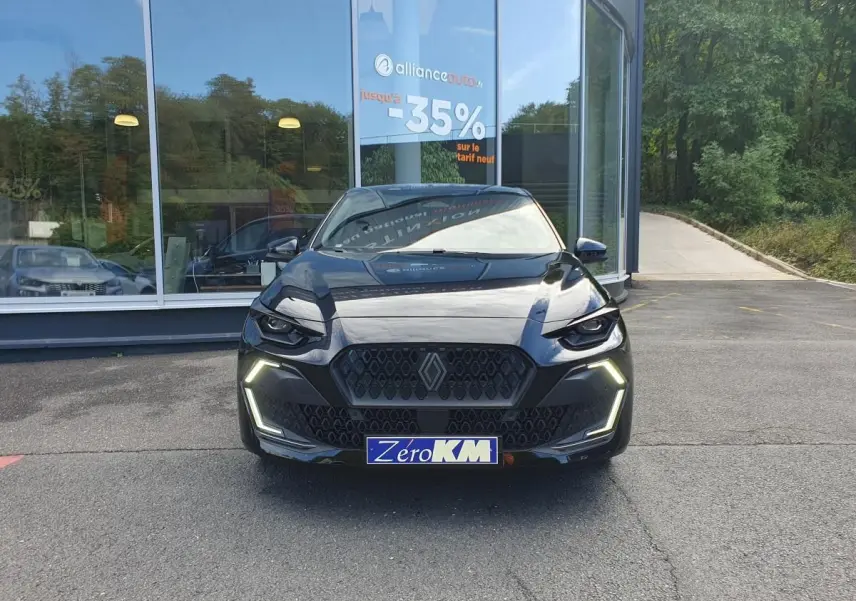 Vue avant d'une Renault Clio VI noire étoile avec feux LED allumés, calandre hexagonale et plaque "Zéro KM" visible.