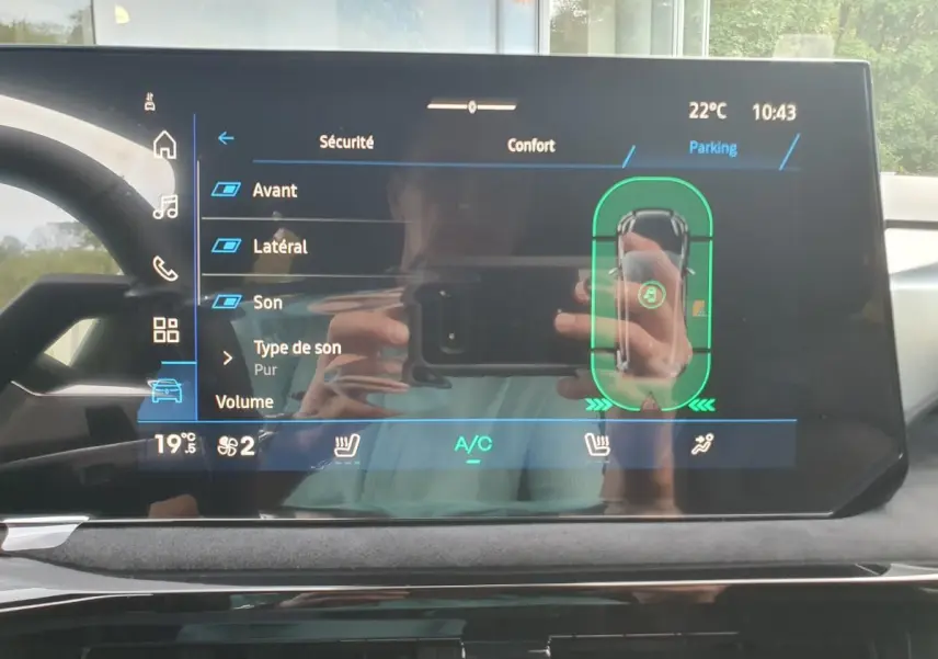 Écran tactile intérieur de la Renault Clio VI affichant les réglages de sécurité et parking, avec reflet du conducteur.