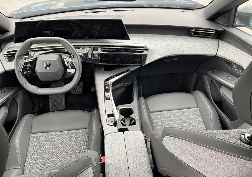 Vue intérieure avant du Peugeot 3008 2025, avec tableau de bord moderne et sièges gris tissu et cuir.