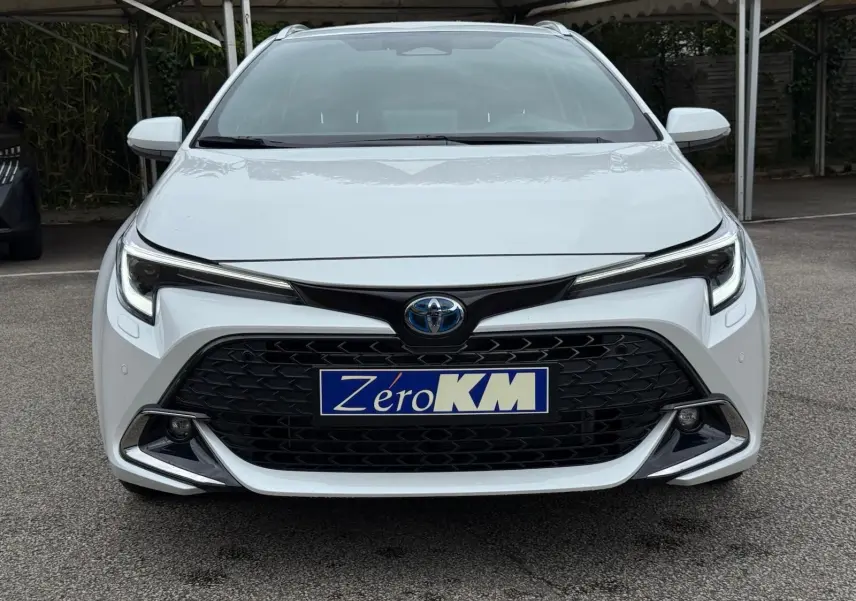 Vue frontale d'une Toyota Corolla Touring Sport blanche lunaire nacrée avec calandre noire et phares LED marqués.