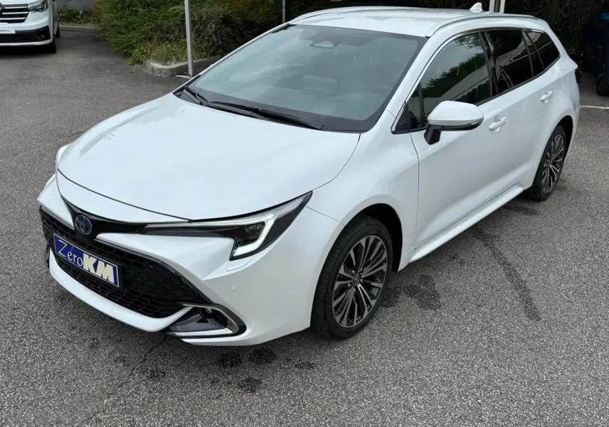 Toyota Corolla Touring Sport blanche nacrée vue en 3/4 avant droit, avec calandre noire et jantes alliage foncé.