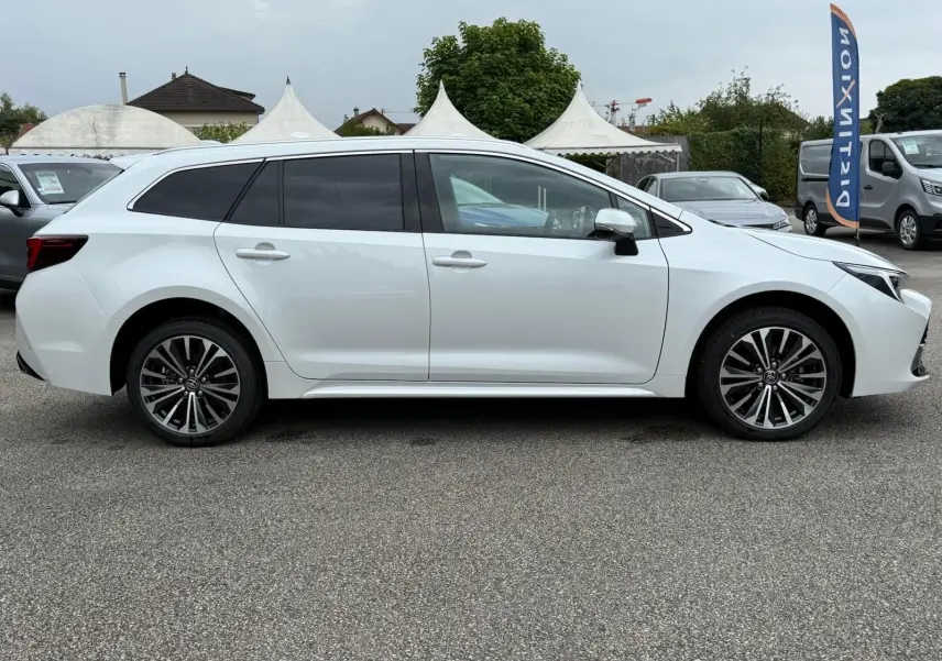 Profil côté gauche d'une Toyota Corolla Touring Sport blanche lunaire nacrée, avec jantes alliage et vitres teintées.