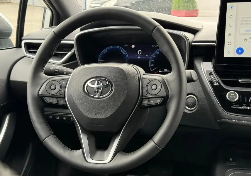 Vue centrée sur le volant noir de la Toyota Corolla Touring Sport 2025, avec tableau de bord numérique et écran tactile visible.