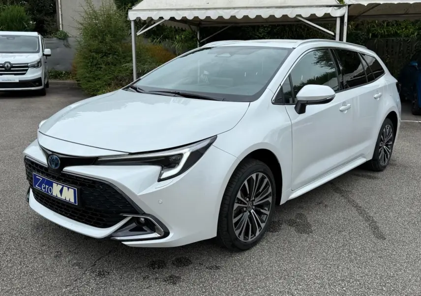 Toyota Corolla Touring Sport blanc lunaire nacré en 3/4 avant droit avec calandre noire et jantes alliage multibranches.