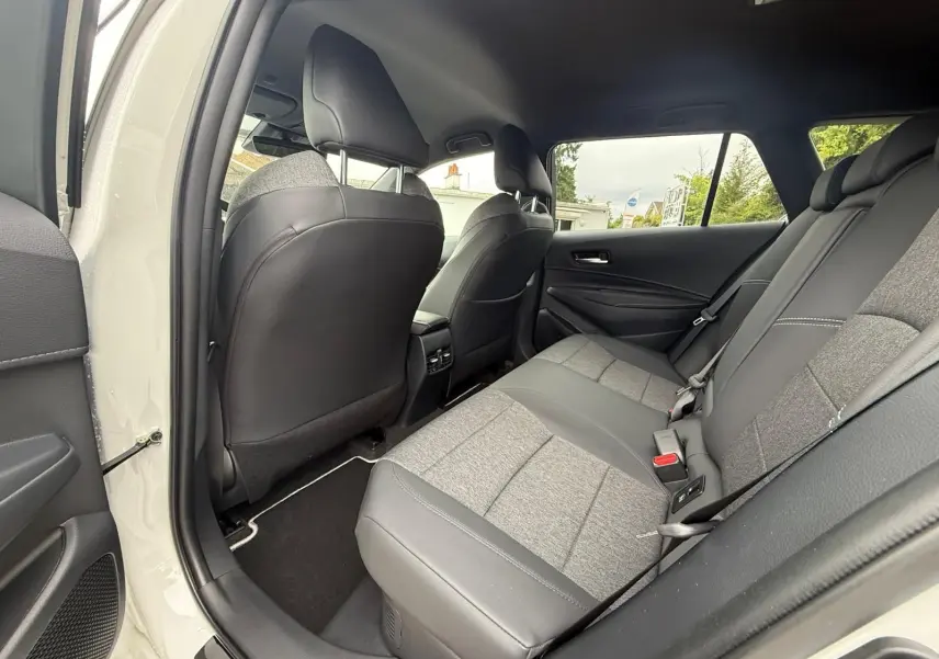 Vue intérieure arrière droite de la Toyota Corolla Touring Sport 2025 blanc lunaire nacré, sièges bi-matière gris et noir.