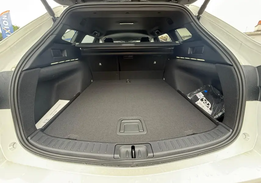 Coffre ouvert vu de l'arrière d'une Toyota Corolla Touring Sport blanche nacrée, montrant un espace de chargement spacieux et propre.